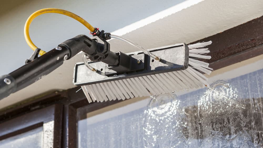 Bilde av en vindusvasker med kost og egen såpedispenser som vasker et vindu fra utsiden - Midt-Norsk Vask AS - Fasadevask